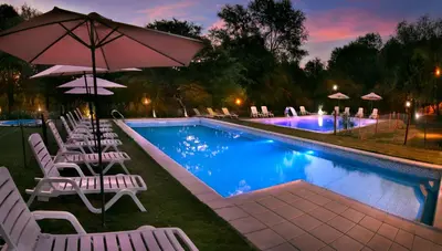 a swimming pool with white chairs and an umbrella at La Faustina Casas de Campo in Villa General Belgrano