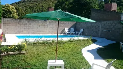 a green umbrella sitting next to a swimming pool at Cabañas Simpson in Santa Rosa de Calamuchita