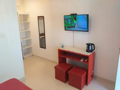 a room with a tv on a wall with a red table at Abuela Mari Apart Cabaña in Villa Cura Brochero