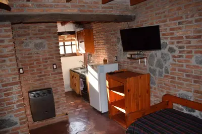 a kitchen with a brick wall with a television and a refrigerator at Cabañas La Rosada in Santa Rosa de Calamuchita