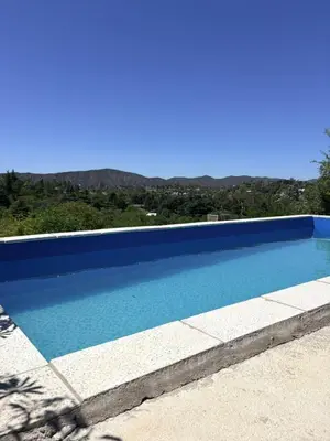 a large blue swimming pool with mountains in the background at Los Frutales in Villa Carlos Paz