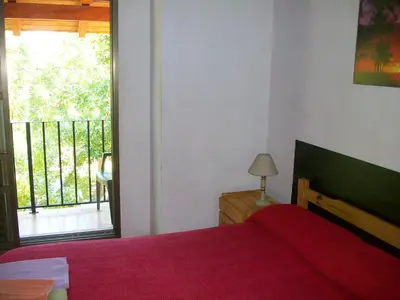 a bedroom with a red bed and a balcony at Hosteria Columbia in Mina Clavero