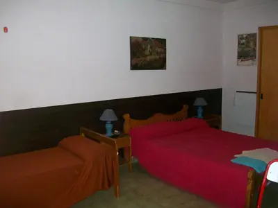 a bedroom with two beds with red sheets and a chair at Hosteria Columbia in Mina Clavero