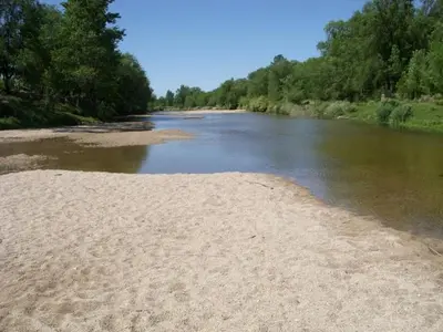 a river with a sandy shore next to trees at Campiranas in Los Reartes