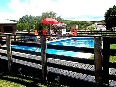 a swimming pool with a red umbrella and chairs at Cabañas mi Sueño in Villa Carlos Paz