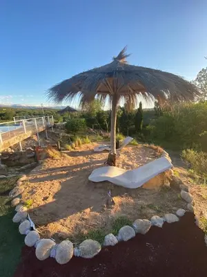 an umbrella sitting on the beach with a bench at Cabañas y Toboganes Rancho la Ñata in Mina Clavero