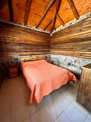 a bed in a wooden room with a red blanket at Cabañas y Toboganes Rancho la Ñata in Mina Clavero