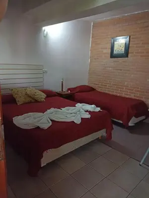 a bedroom with two beds with red sheets and a brick wall at Complejo Navi in Mina Clavero