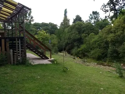 a wooden bridge over a grass field with trees at Cabaña Atha Iti in Villa General Belgrano