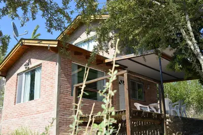 a brick house with a wrap around porch at Cabañas Kumelkalechi in Los Reartes
