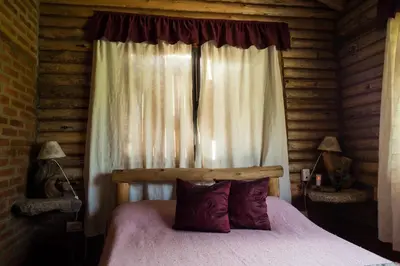 a bed in a log cabin with a window at Cabañas Quisama in Nono