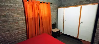 a bedroom with orange curtains and a brick wall at El Campito casa frente al río in Villa Carlos Paz