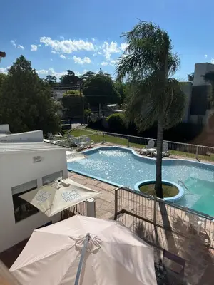 a swimming pool with two umbrellas and a palm tree at Casa Piedra Hotel in Villa Carlos Paz
