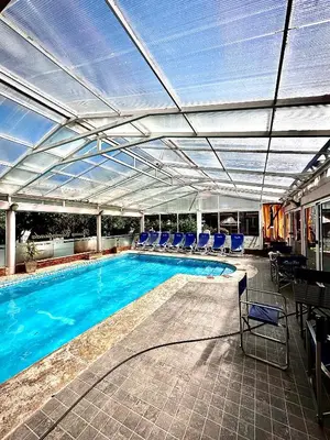 a swimming pool with a retractable roof and blue chairs at Apart Hotel Piscu Yaco in Merlo