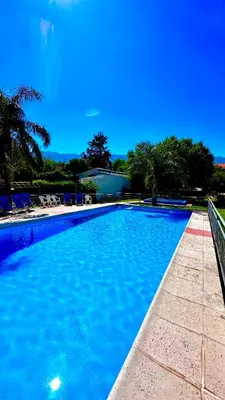 a large blue swimming pool with chairs and trees at Apart Hotel Piscu Yaco in Merlo