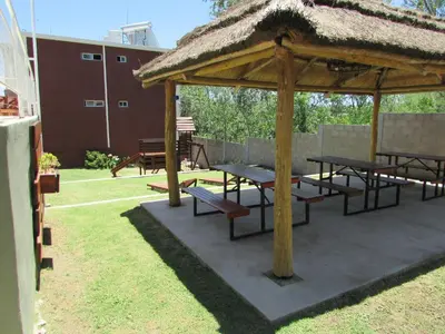 a pavilion with picnic tables and a straw roof at La Villa Inn in Villa Carlos Paz