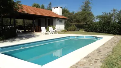 a swimming pool with two chairs and a house at Entre Sierras in Villa General Belgrano