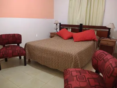 a bedroom with a bed with red pillows and two chairs at Complejo ARABELA in Merlo