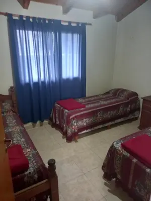 a room with two beds and a window with blue curtains at Complejo Camila in Villa Carlos Paz