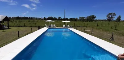 a blue swimming pool with chairs and umbrellas at Posta Suites Apart - Los Reartes in Los Reartes