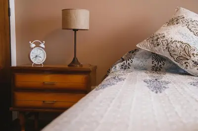 a bed with a nightstand with a clock on it at 4 PERSONAS A 150 Mts SANATORIO ALLENDE in Cordoba