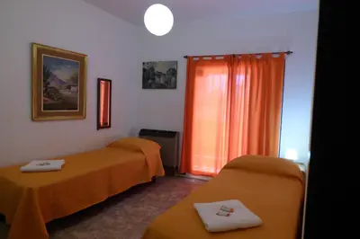 a room with two beds and a window with orange sheets at Departamento Centrico in Villa Carlos Paz
