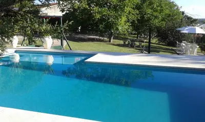 a blue swimming pool with a table and an umbrella at Belvedere Hotel para Adultos in Santa Rosa de Calamuchita