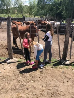 two girls and a woman looking at horses at a fence at El Zuriaco in Santa Rosa de Calamuchita