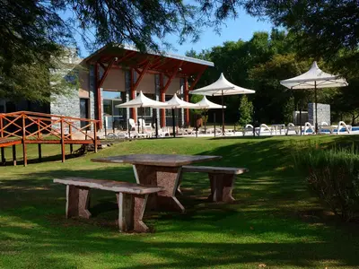 a picnic table and benches in a park with umbrellas at Posada Piedras Del Sol in Villa General Belgrano