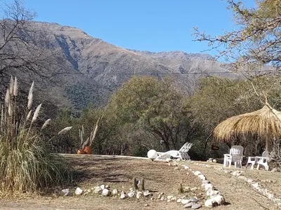 a field with two chairs and a huts and mountains at Mainame Traslasierra in Los Hornillos