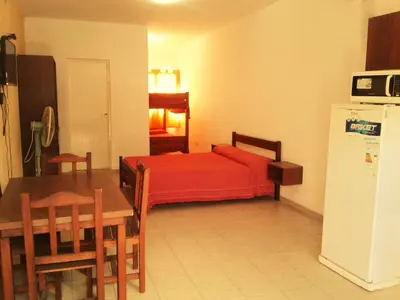 a bedroom with a bed and a table and a refrigerator at Departamentos Flor de Loto in Mina Clavero