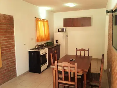 a kitchen with a table and a stove and refrigerator at Departamentos Flor de Loto in Mina Clavero