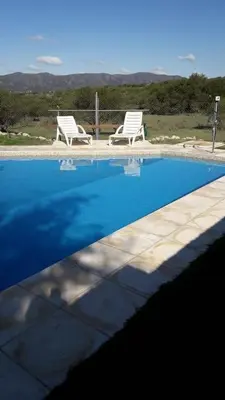 a swimming pool with two white chairs at Cabañas Doña Itati in Villa Carlos Paz