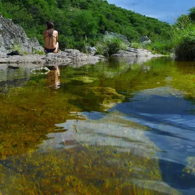 a woman in a bikini sitting on a rock next to a river at Arroyo Escondido in La Cumbrecita