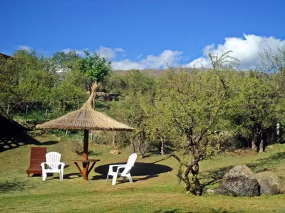 two white chairs and a table and a straw umbrella at Cabañas Toay Merlo San Luis in Merlo