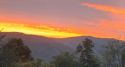 a sunset in the mountains with trees in the foreground at CABAÑA-alojamiento ATAIAS in Santa Rosa de Calamuchita