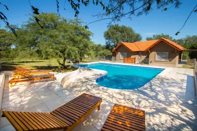 a swimming pool with benches and a house at El Refugio Casas de Campo in Villa General Belgrano