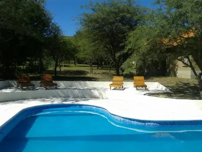 a swimming pool with two chairs and a group of trees at El Refugio Casas de Campo in Villa General Belgrano