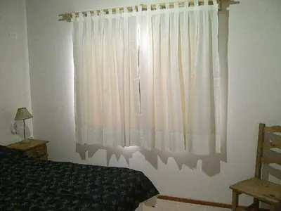 a bedroom with a bed and a window with white curtains at El Refugio Casas de Campo in Villa General Belgrano