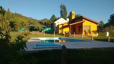 a swimming pool in front of a yellow house at Cabañas Lomas de Calamuchita in Santa Rosa de Calamuchita