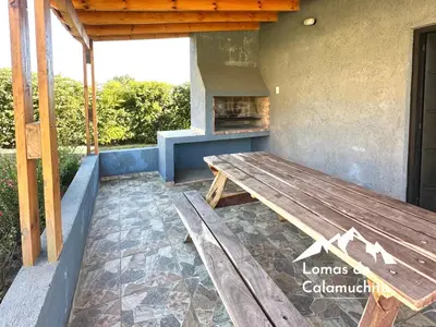 a wooden picnic table on a patio with a fireplace at Cabañas Lomas de Calamuchita in Santa Rosa de Calamuchita