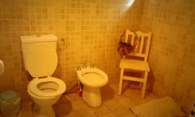 a bathroom with a toilet and a wooden chair at Abbá Departamentos in Mina Clavero