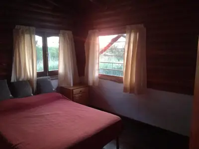 a bedroom with a red bed and two windows at Cabañas Buen Ayre in Villa Rumipal