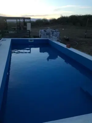 a large blue swimming pool with the sunset in the background at Cabañas Buen Ayre in Villa Rumipal