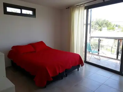 a bedroom with a red bed and a balcony at Departamento LA PAZ in Villa Carlos Paz