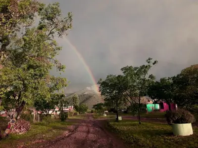 a rainbow in the sky over a dirt road at Sierra Magenta in Los Hornillos
