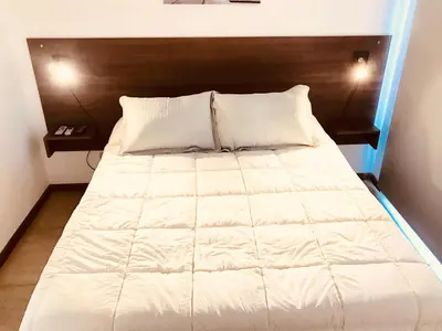 a large white bed with a wooden head board at BOULEVARD departamentos in Mina Clavero