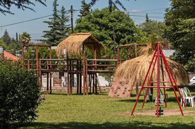 a playground with a swing set and a hut at Hotel Parque Siquiman in Villa Carlos Paz