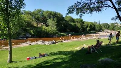 a group of people sitting in a park next to a river at Duplex a mts del Rio con Aire Acond in Villa Carlos Paz