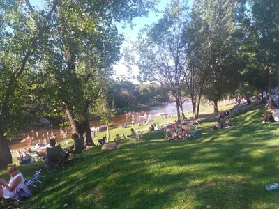a group of people sitting in the grass near a river at Duplex a mts del Rio con Aire Acond in Villa Carlos Paz